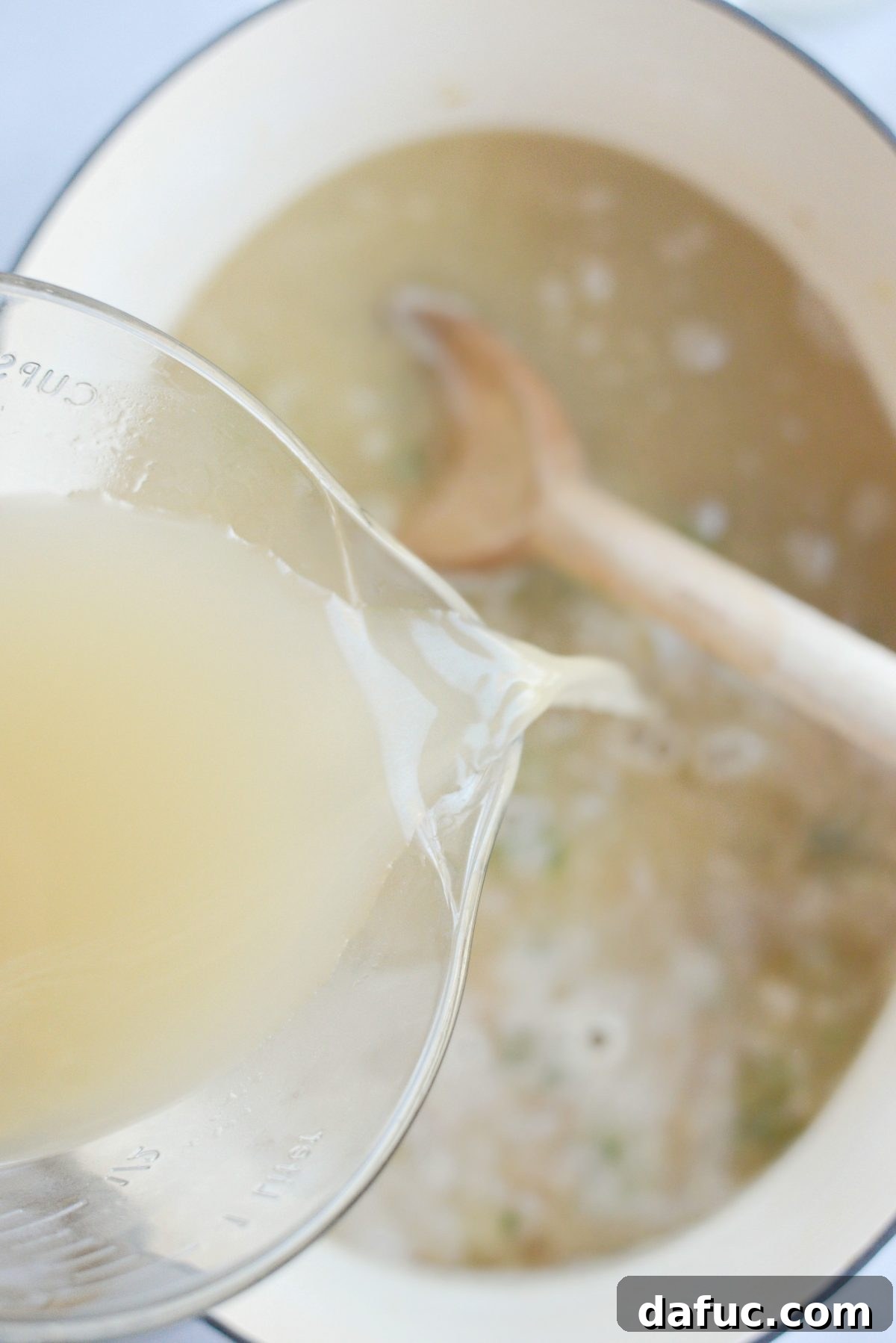 Chicken broth being poured into the simmering beer and vegetable base in the Dutch oven.