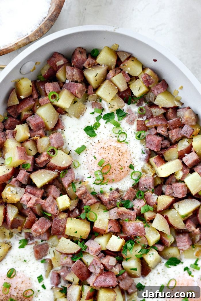 Corned beef hash with baked eggs garnished with fresh herbs and seasoning, ready for serving.