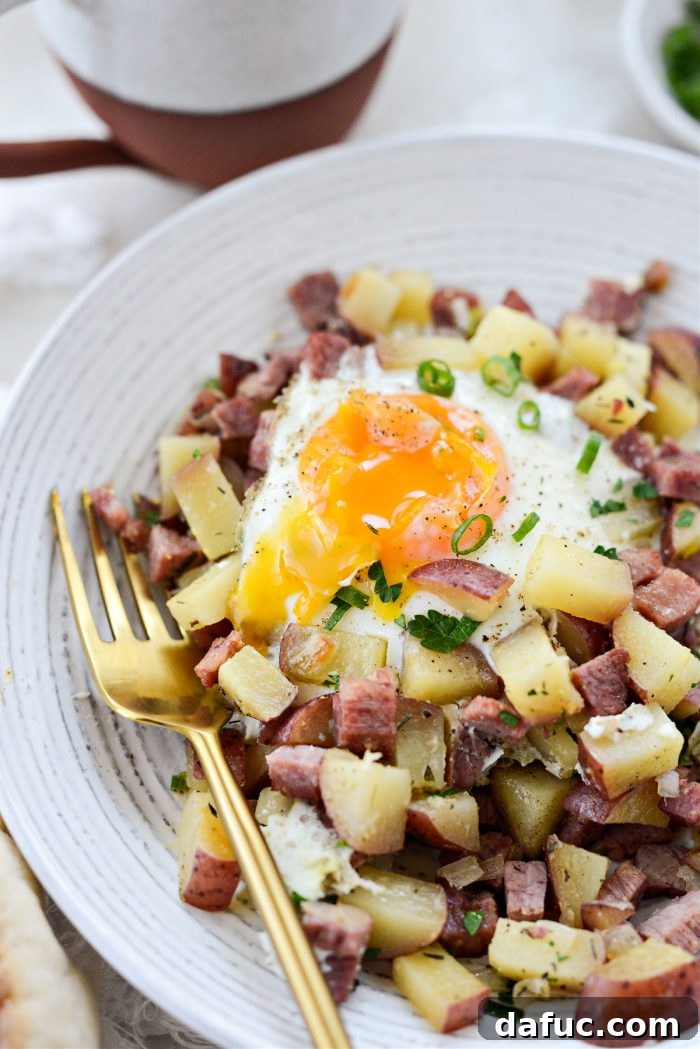 A close-up of a single serving of corned beef hash with egg and fresh parsley on a white plate.