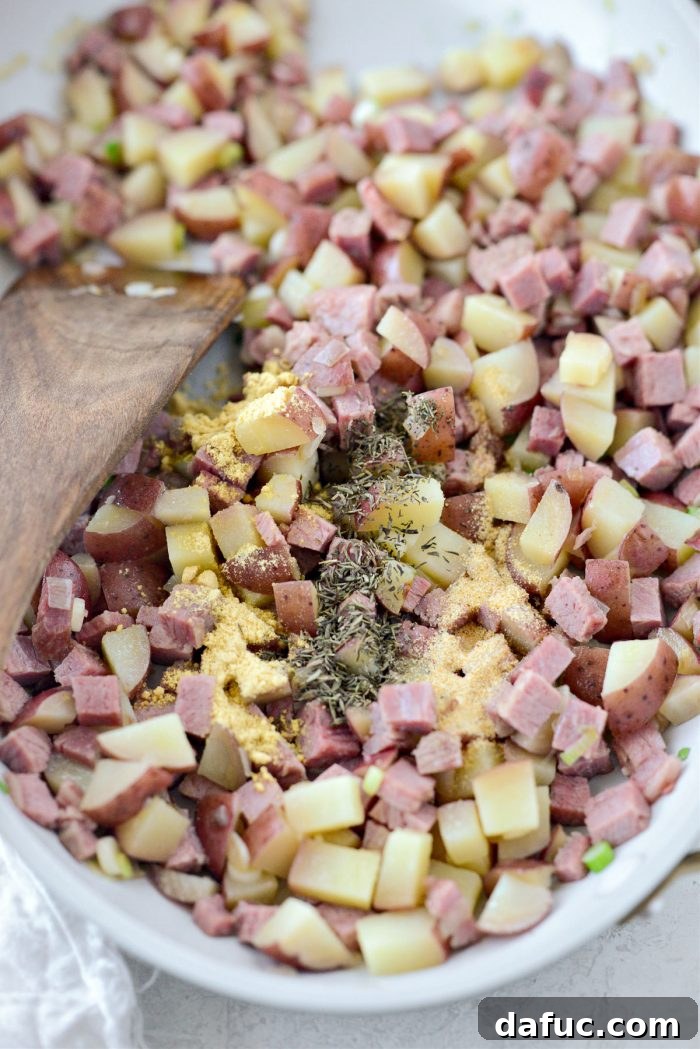 Hash mixture being seasoned with dried mustard, thyme, and garlic powder, then stirred to combine.