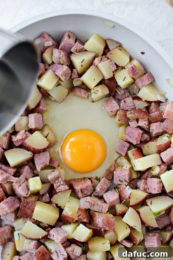 Cracked eggs being gently poured into the wells created in the corned beef hash.