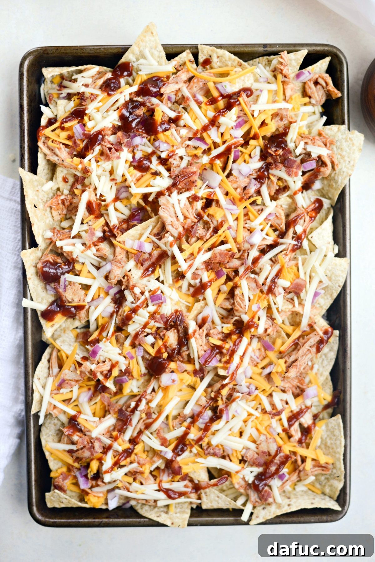 Topping nachos with more cheese, red onions, bacon, and a drizzle of BBQ sauce.