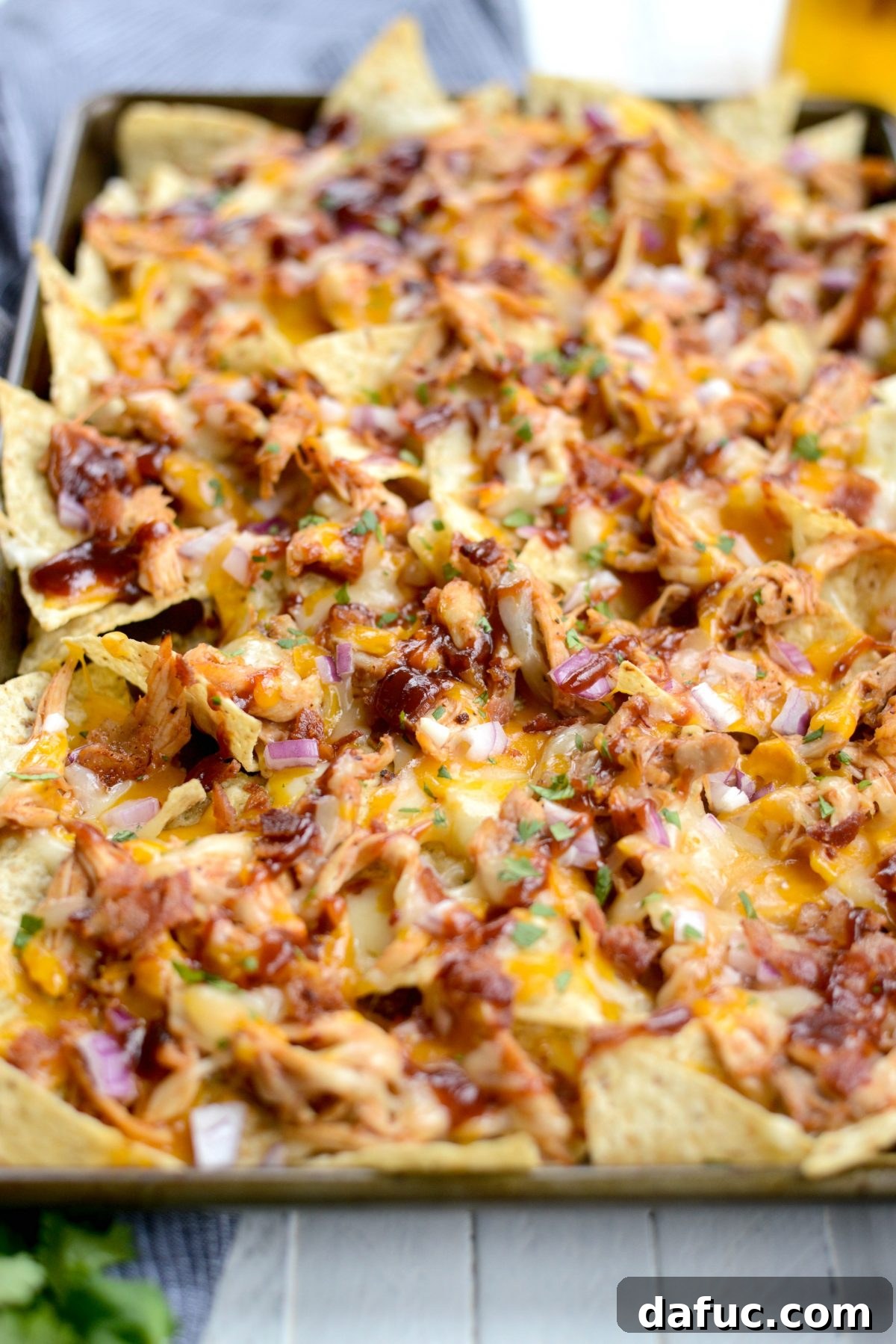 Sheet Pan BBQ Chicken Nachos with melted cheese, chicken, bacon, and red onion.