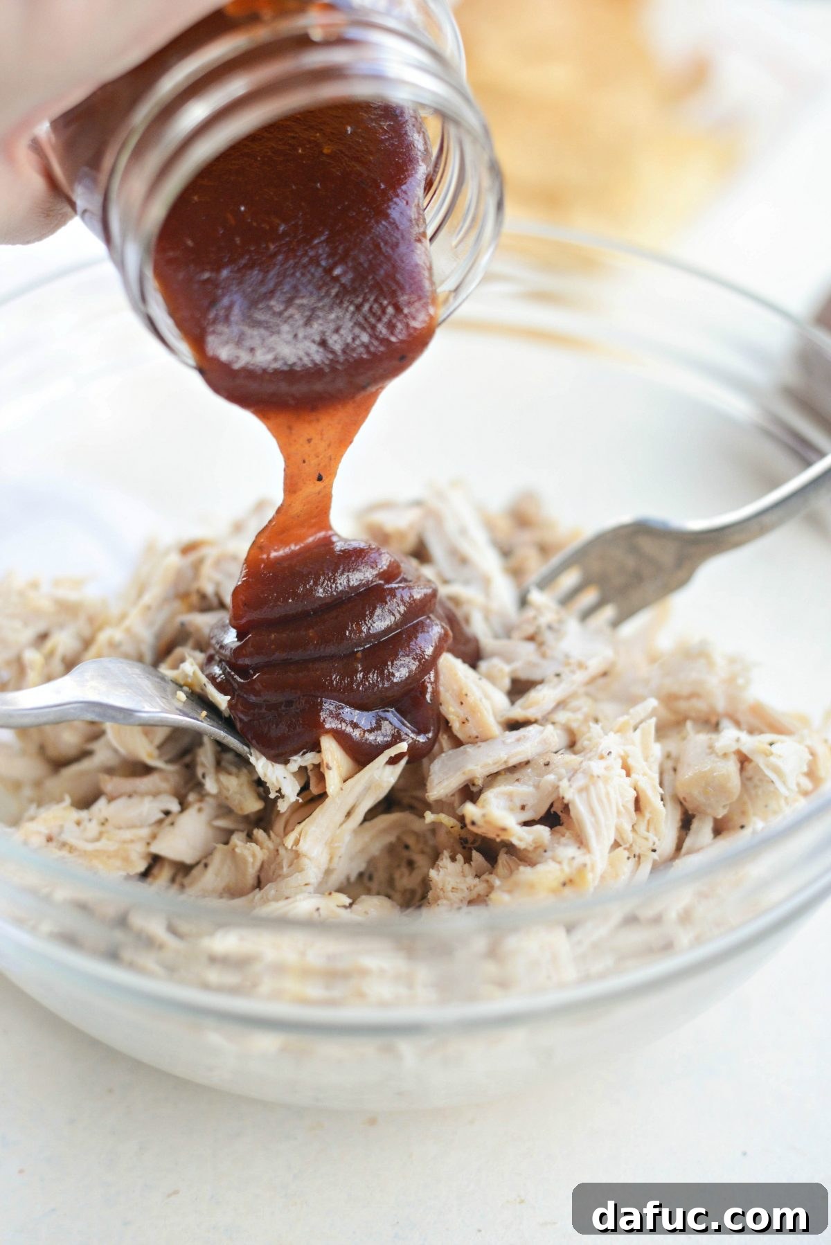 Pouring sweet barbecue sauce over shredded chicken.
