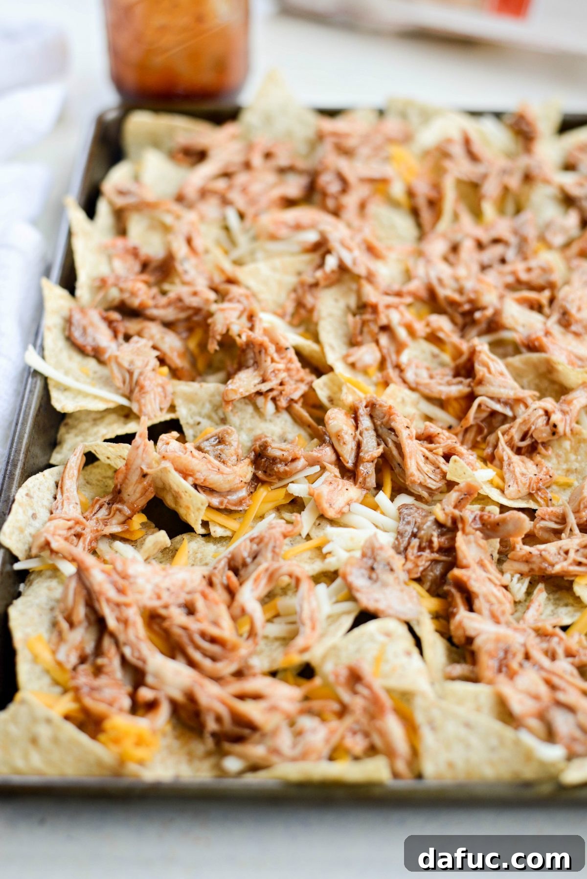 Adding cheese and saucy BBQ chicken to tortilla chips.