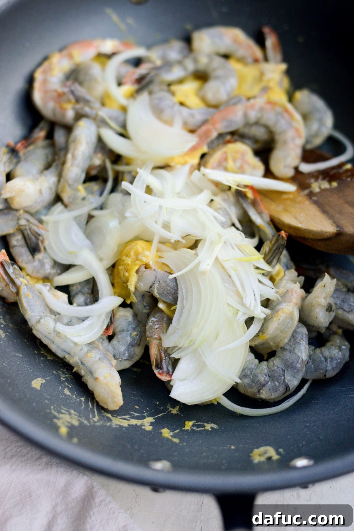 Adding shrimp and onions to scrambled eggs in a wok