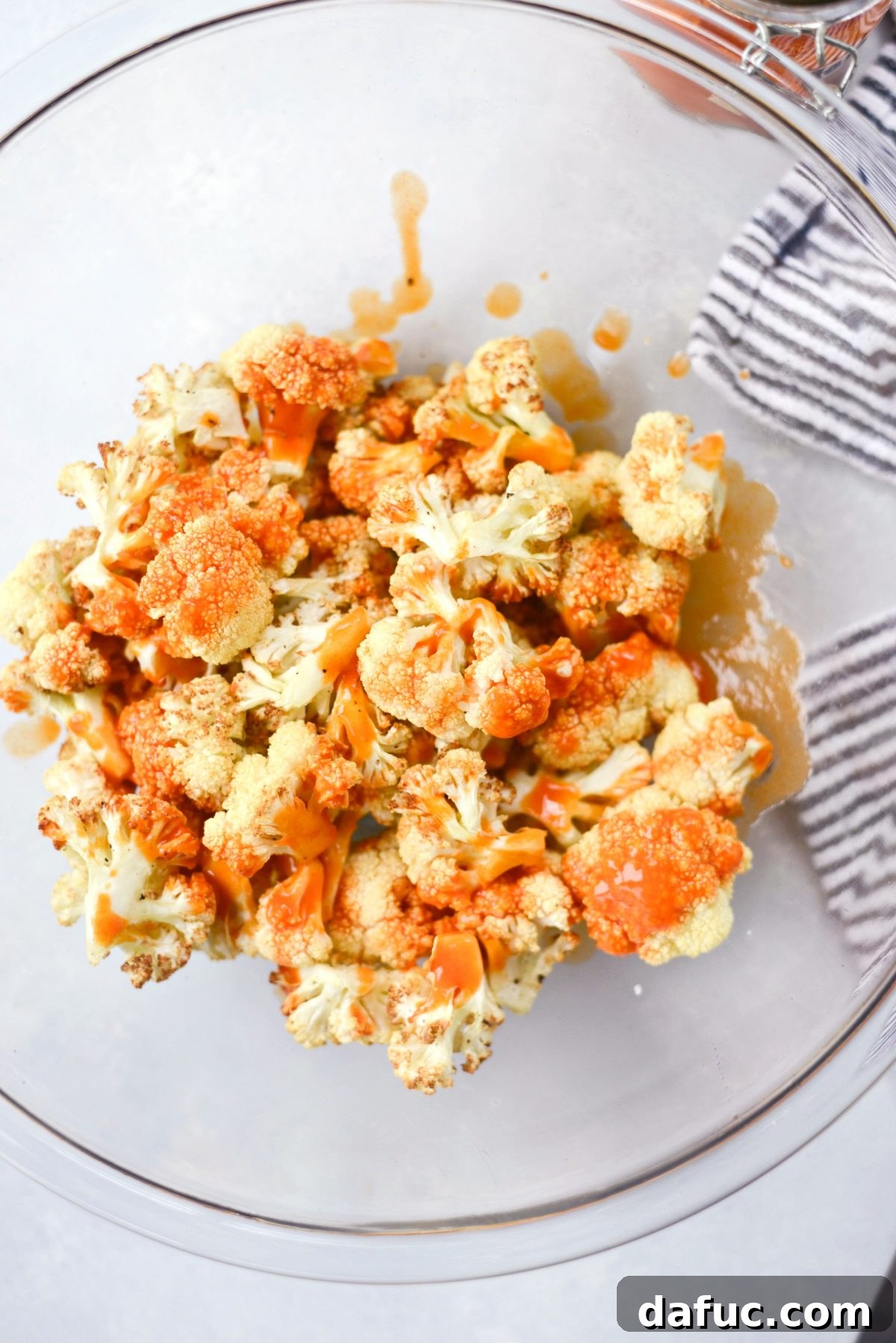 Drizzling buffalo sauce over air-fried cauliflower