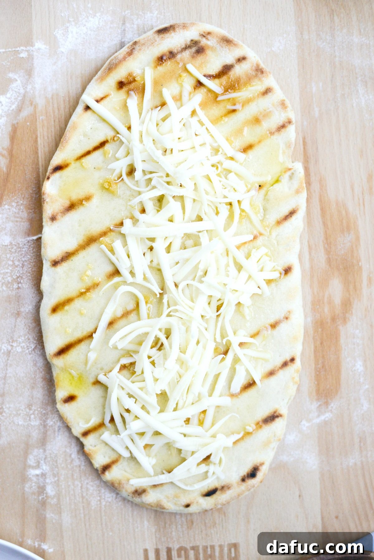 Grilled pizza dough topped with garlic oil and shredded cheese, ready for more toppings