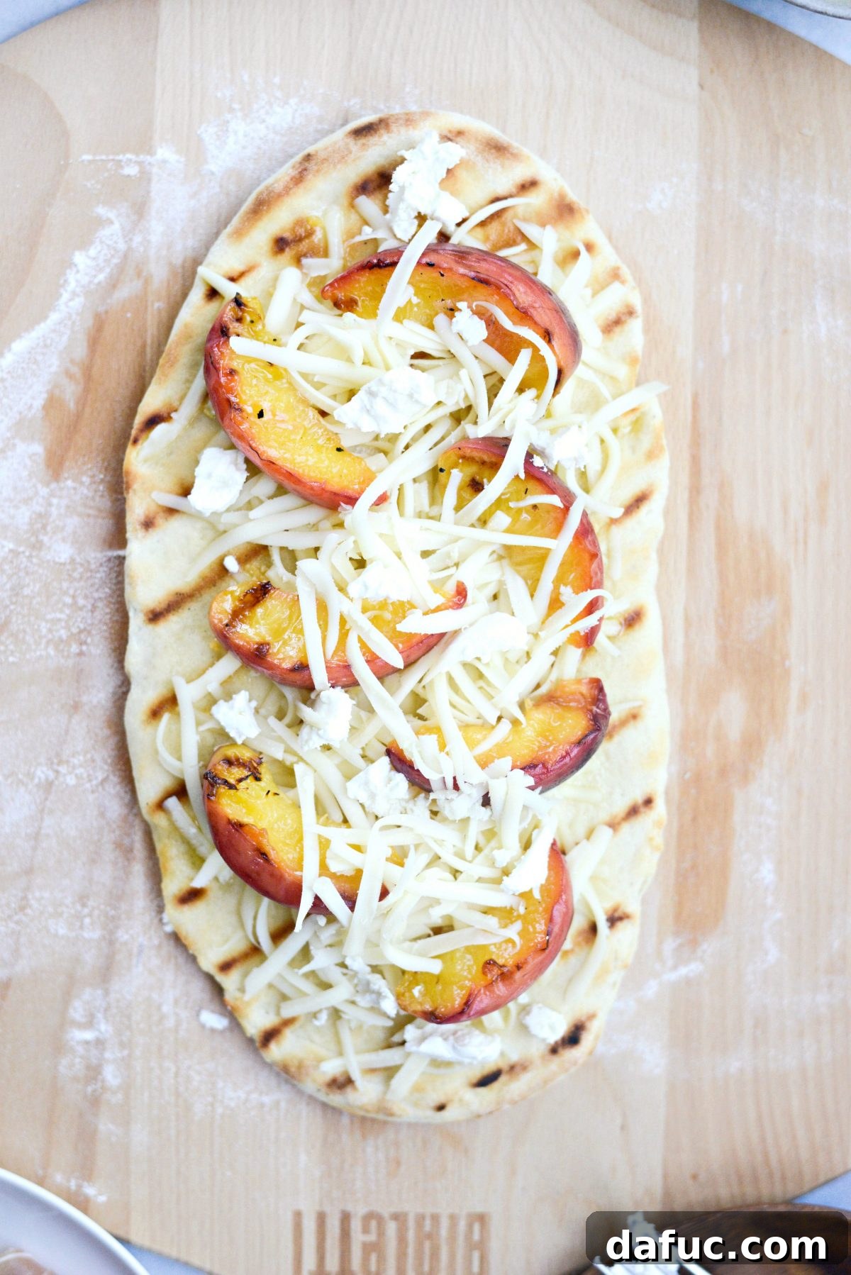 Flatbread topped with grilled peaches, goat cheese, and mozzarella, ready for final grill