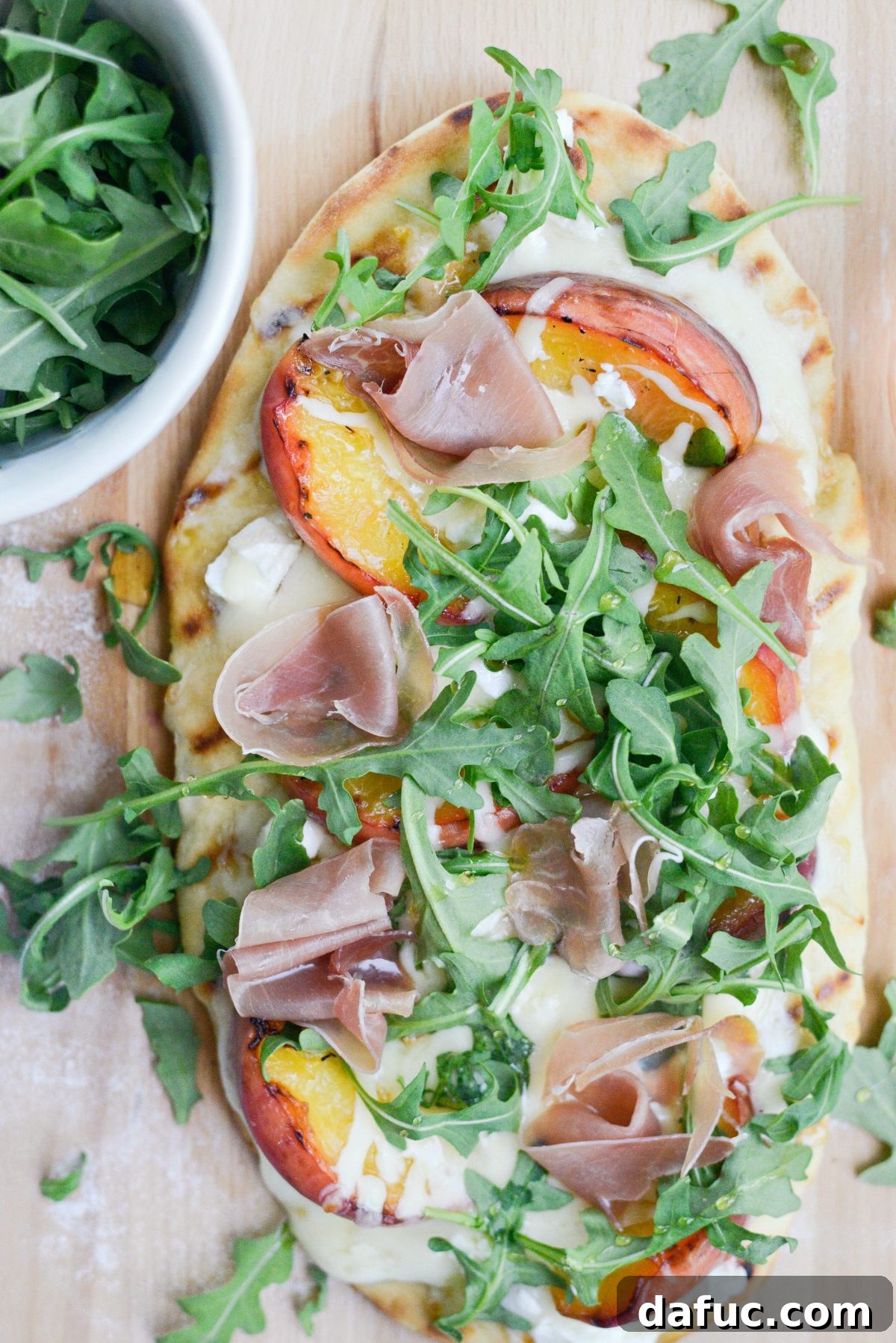Grilled flatbread with peaches, goat cheese, prosciutto, and arugula, being drizzled with honey