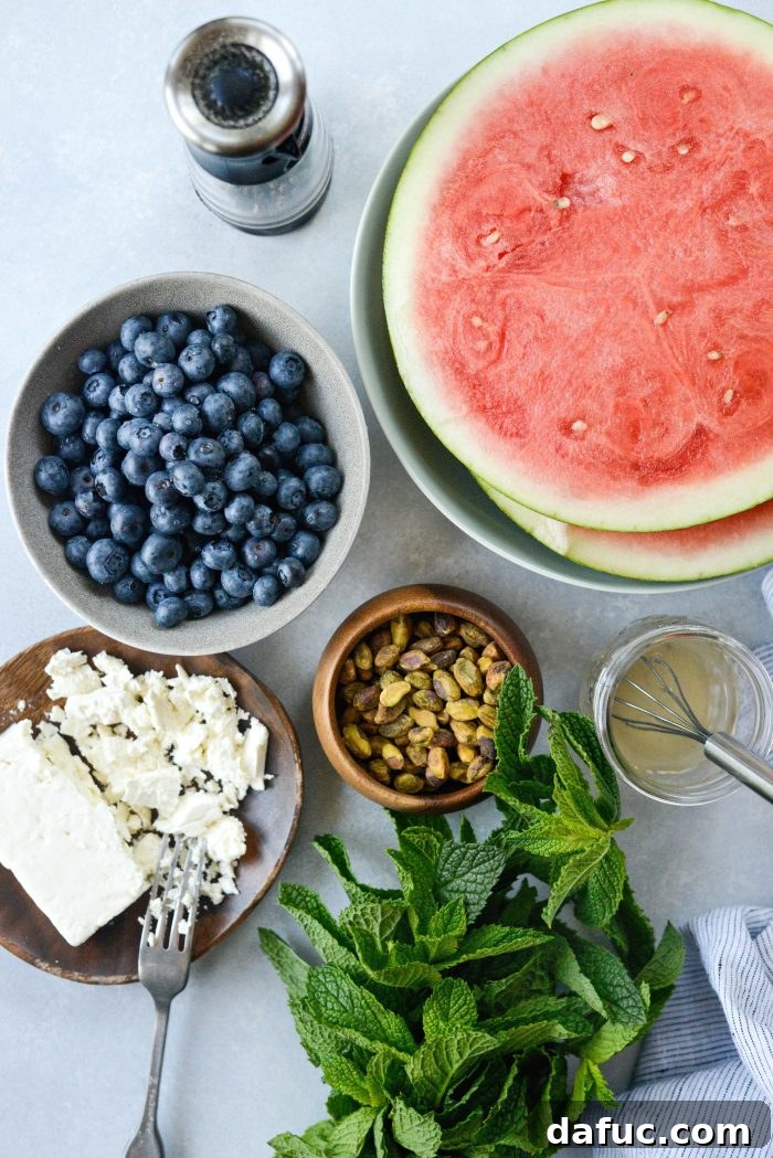 Ingredients laid out for Watermelon Blueberry Feta Salad: watermelon, blueberries, feta, mint, pistachios, and vinaigrette.