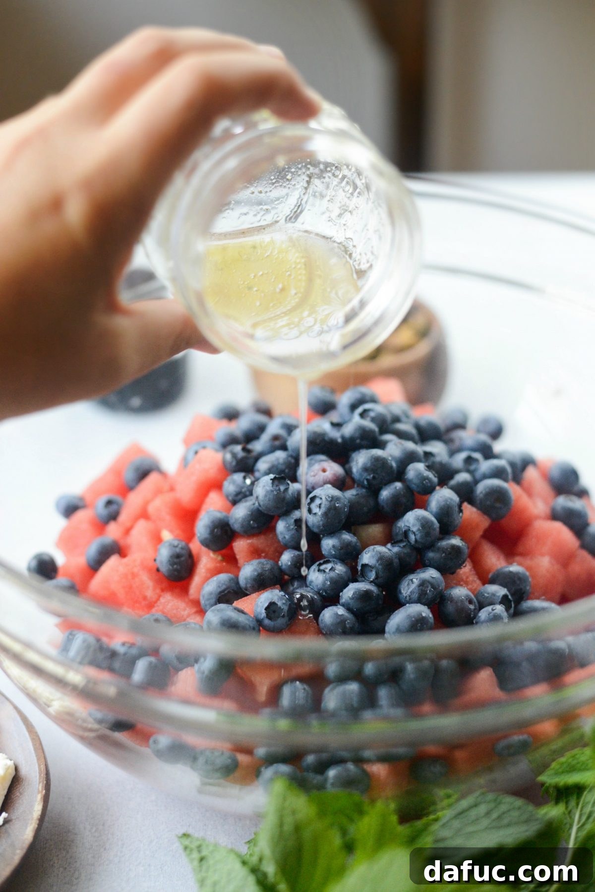 Drizzling champagne vinaigrette over watermelon and blueberries in a bowl.