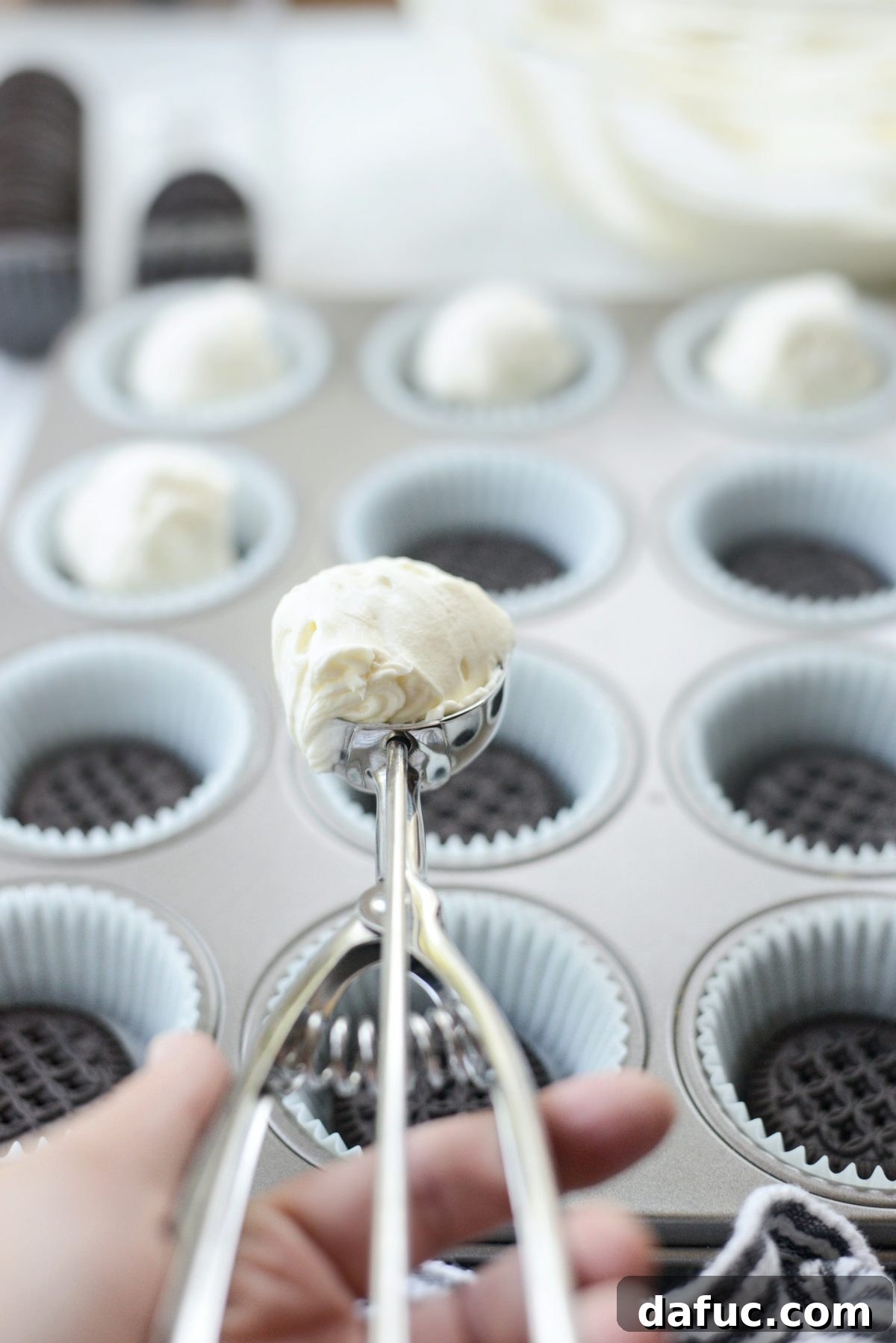 Decadent No-Bake Cookies and Cream Cheesecake Bites 11 Scooping the creamy cheesecake filling over a cookie base in a muffin liner using a measuring scoop