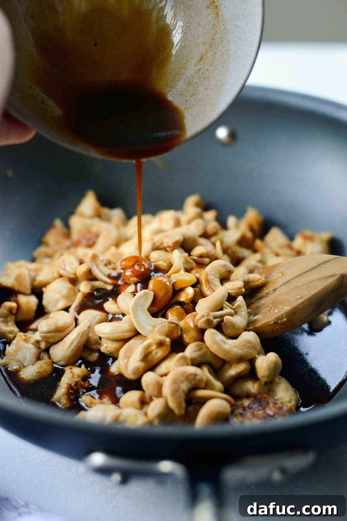 Adding toasted cashews and stir-fry sauce to the cooked chicken.