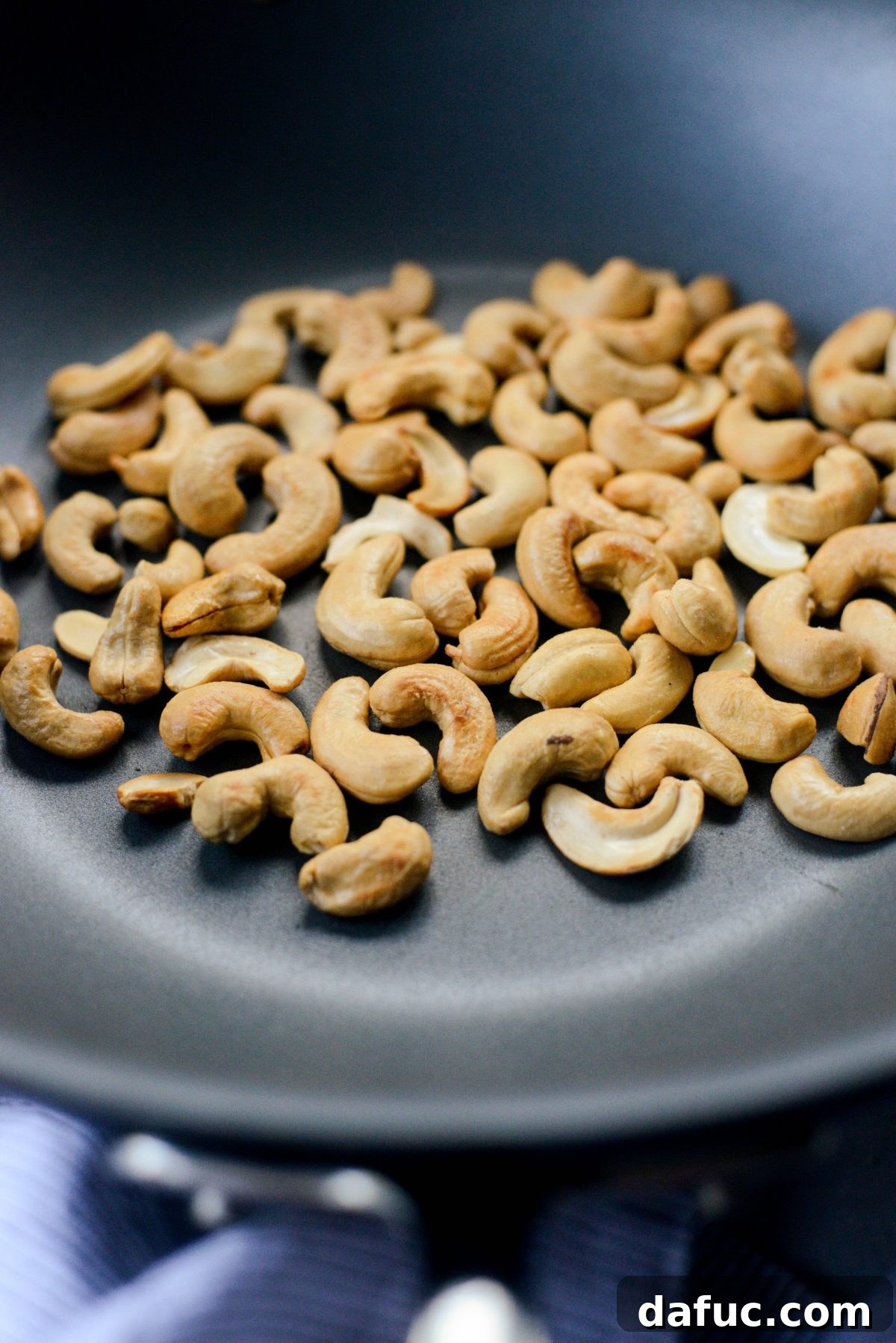 Toasting cashews in a wok until fragrant and golden.