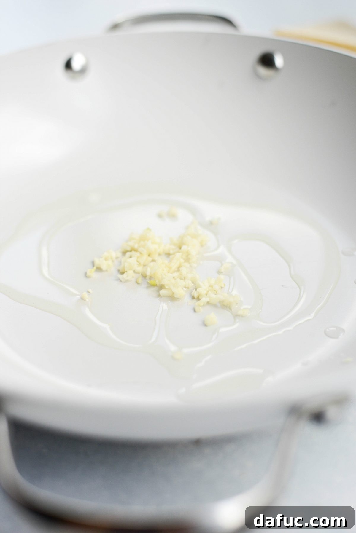 Olive oil being heated with minced garlic in a non-stick skillet