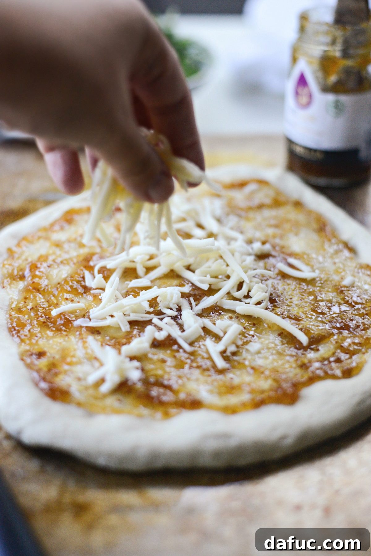 Sprinkling fontina cheese over fig jam pizza