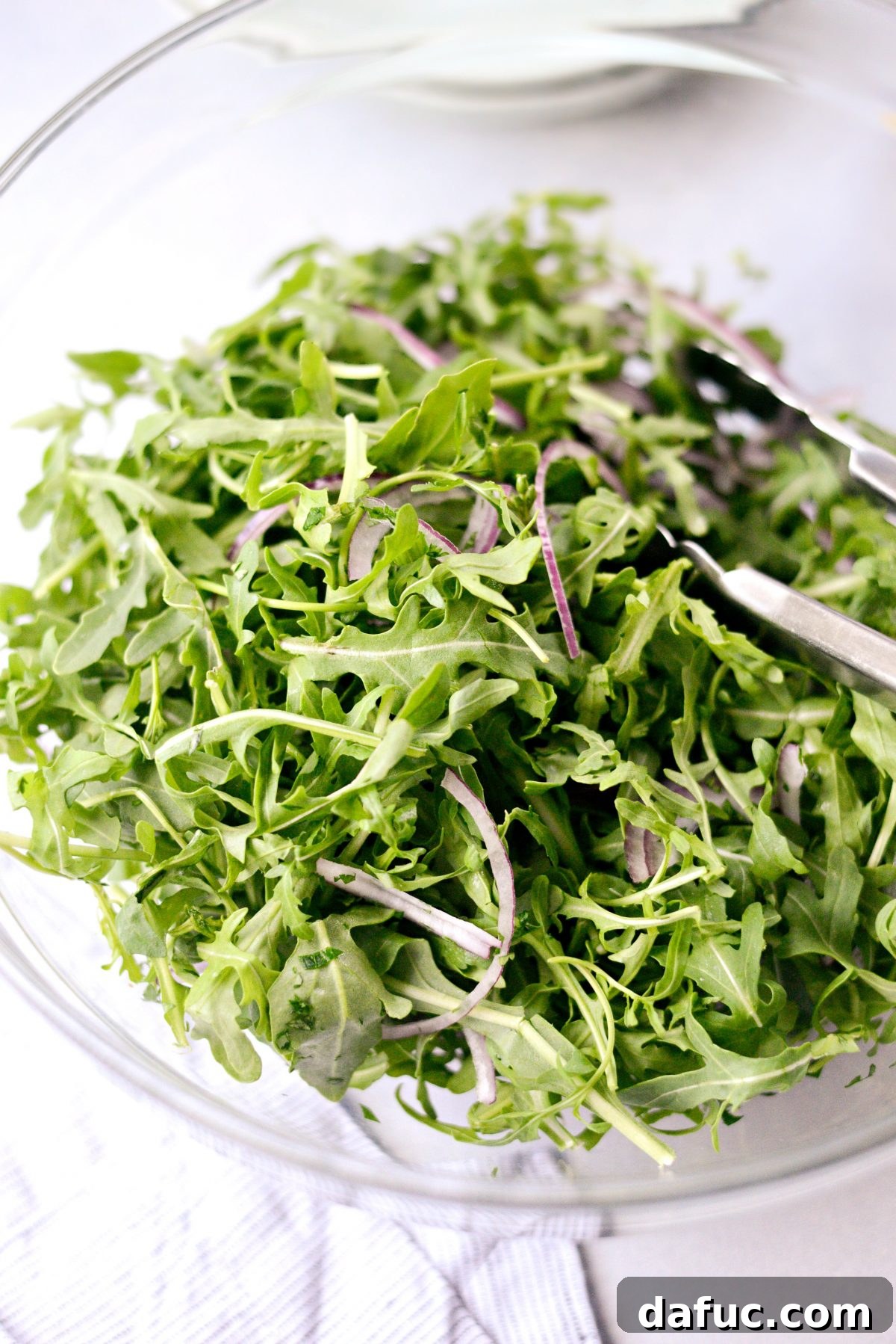 Shawarma Roasted Cauliflower & Chickpea Bowl 11 Hands gently tossing arugula, red onion, and herbs in a bowl