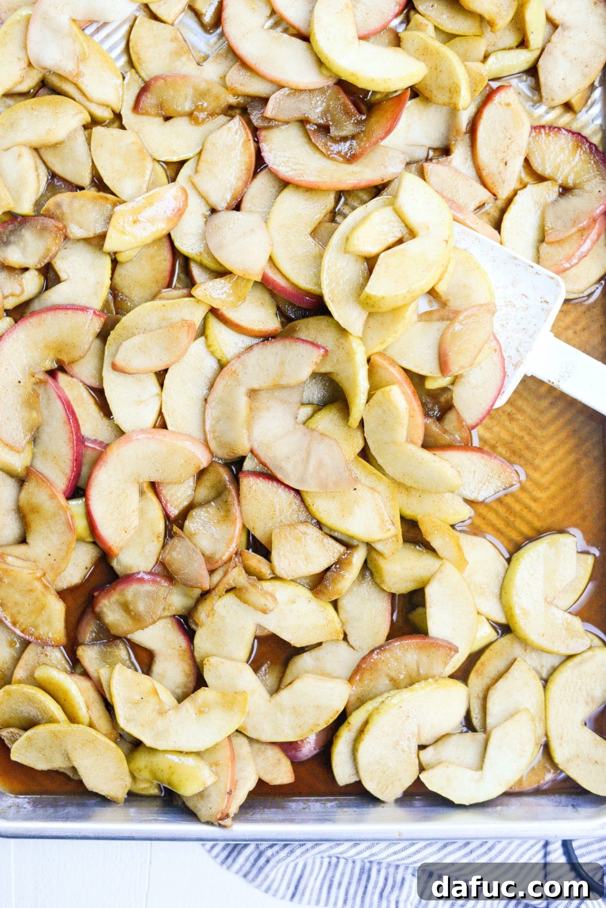 Cooked apples spread out on a rimmed metal baking sheet to cool