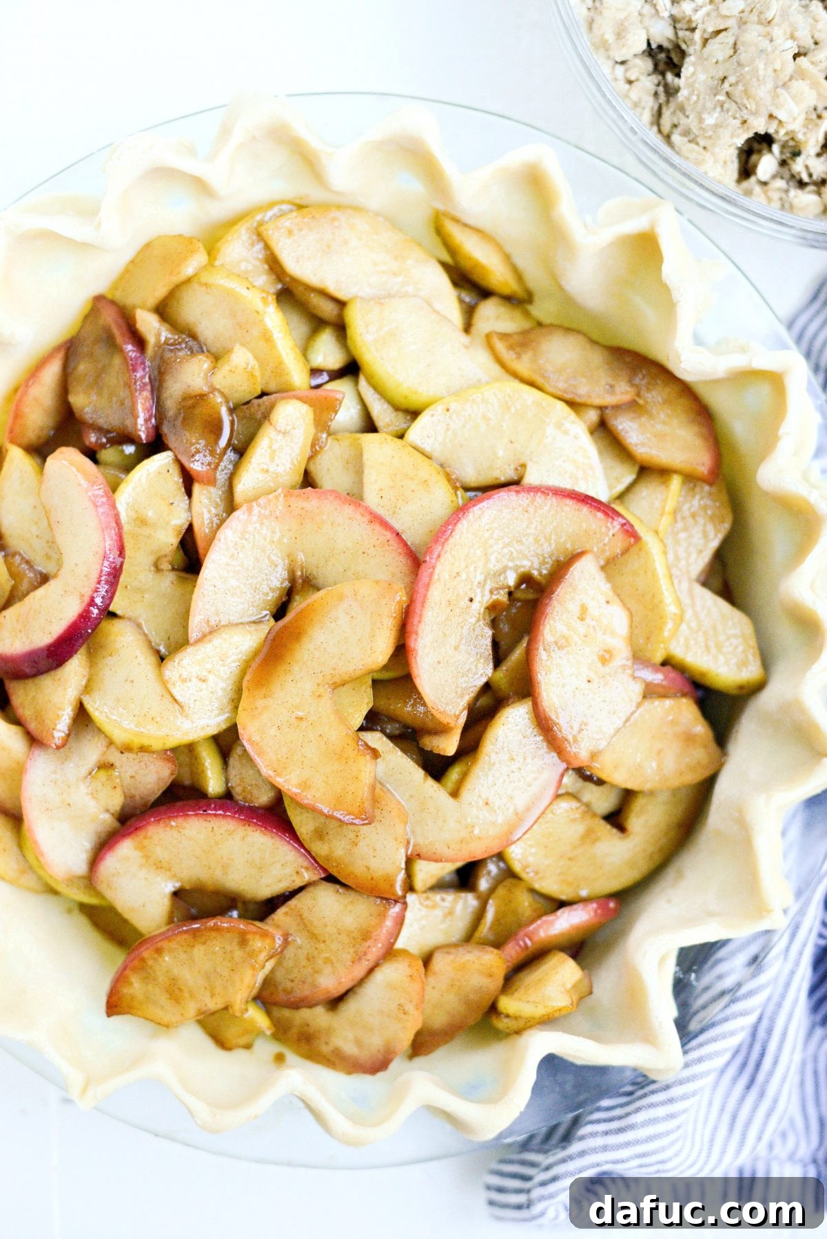 Cooled apple filling being added to the uncooked pie dough in the dish
