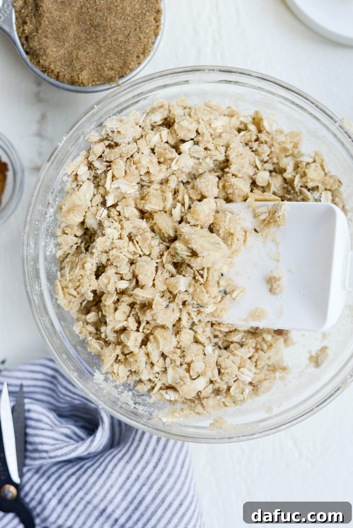 Mixture being stirred to combine oats, flours, sugar, and melted butter
