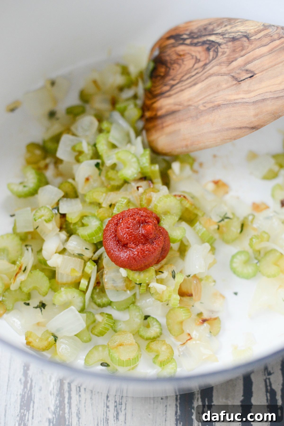 A dollop of rich tomato paste added to the sautéed aromatics, ready to be stirred and caramelized.