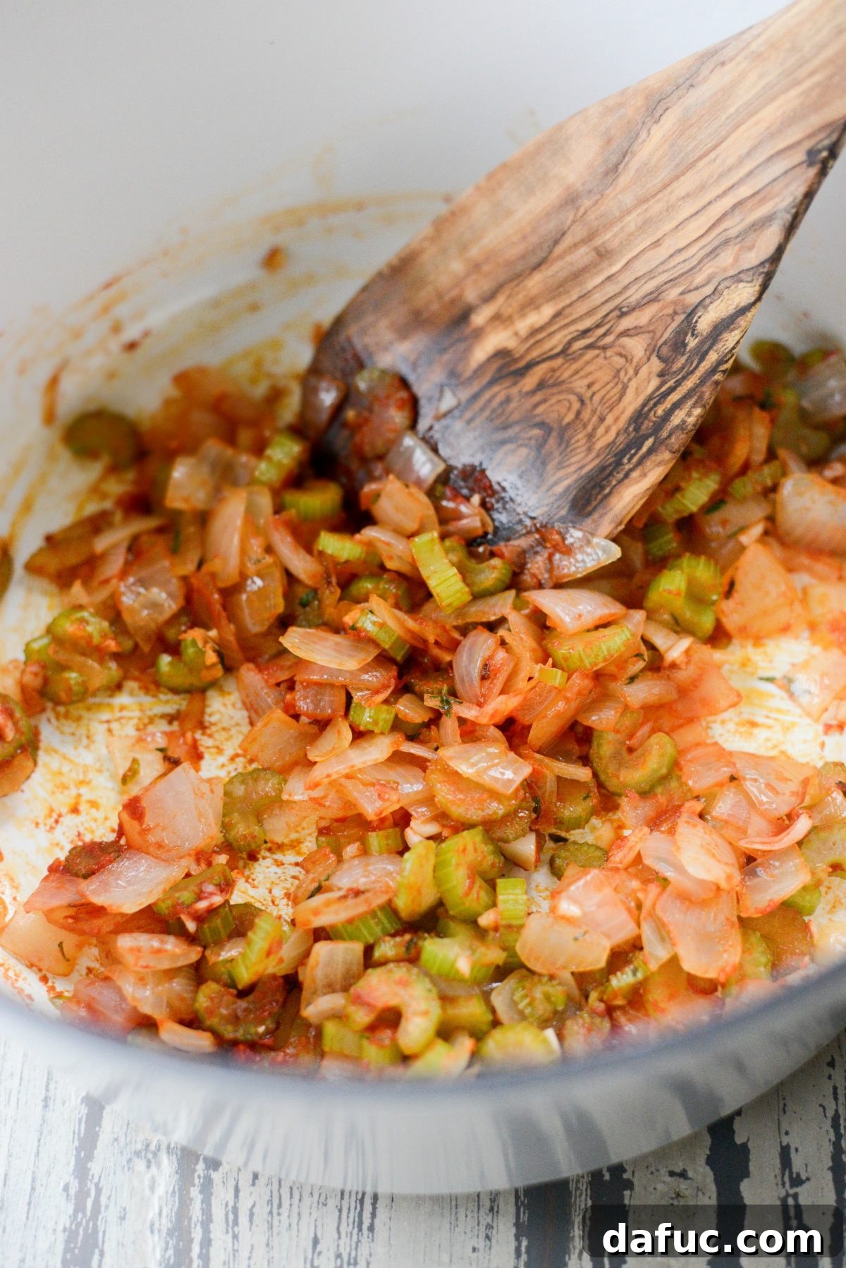 Tomato paste being stirred into the sautéed vegetables, caramelizing and deepening its rich flavor.