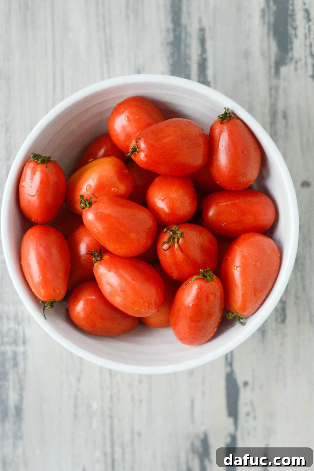 A bowl overflowing with freshly picked mini Roma tomatoes, ready for roasting.