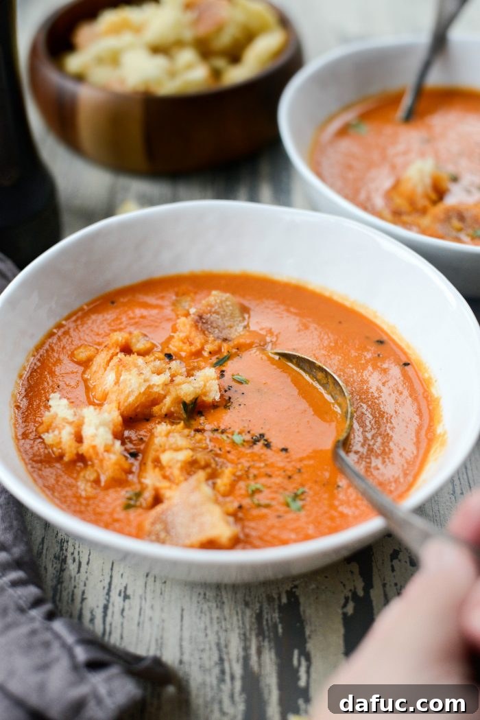 A comforting bowl of Homemade Roasted Red Pepper Tomato Soup, garnished with fresh thyme and a swirl of cream.