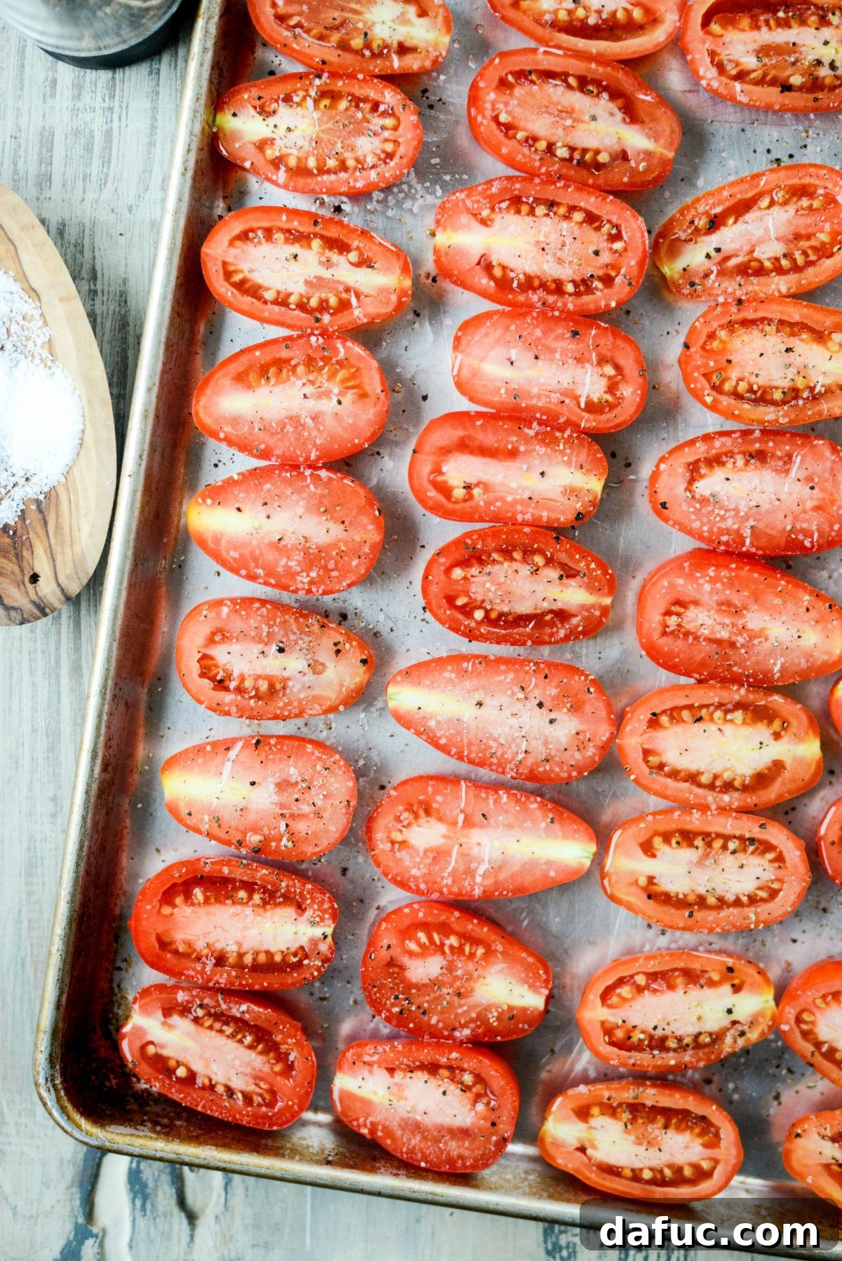 Halved Roma tomatoes drizzled with olive oil and seasoned with salt and pepper on a baking sheet, ready for roasting.