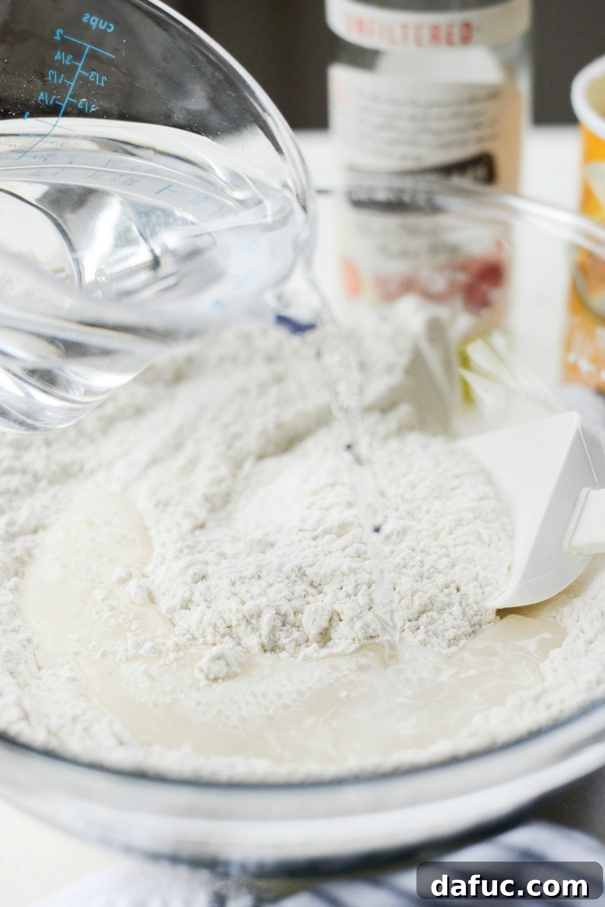 No-Knead Ciabatta: Easy Homemade Perfection 7 Pouring water into a bowl with whisked dry ingredients for ciabatta dough