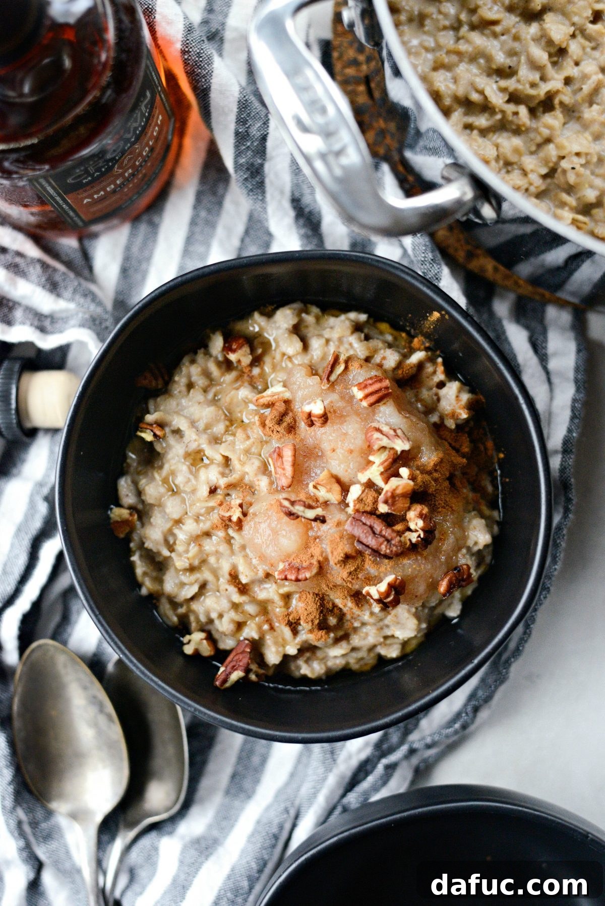 A serving of Apple Chai Oatmeal in a stylish black bowl, garnished with applesauce, maple syrup, and pecans.