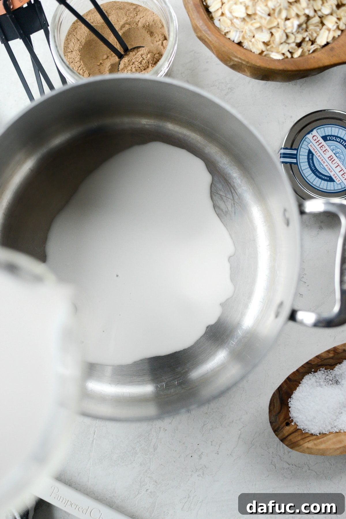 Pouring almond milk into a saucepan on the stove, beginning the oatmeal cooking process.
