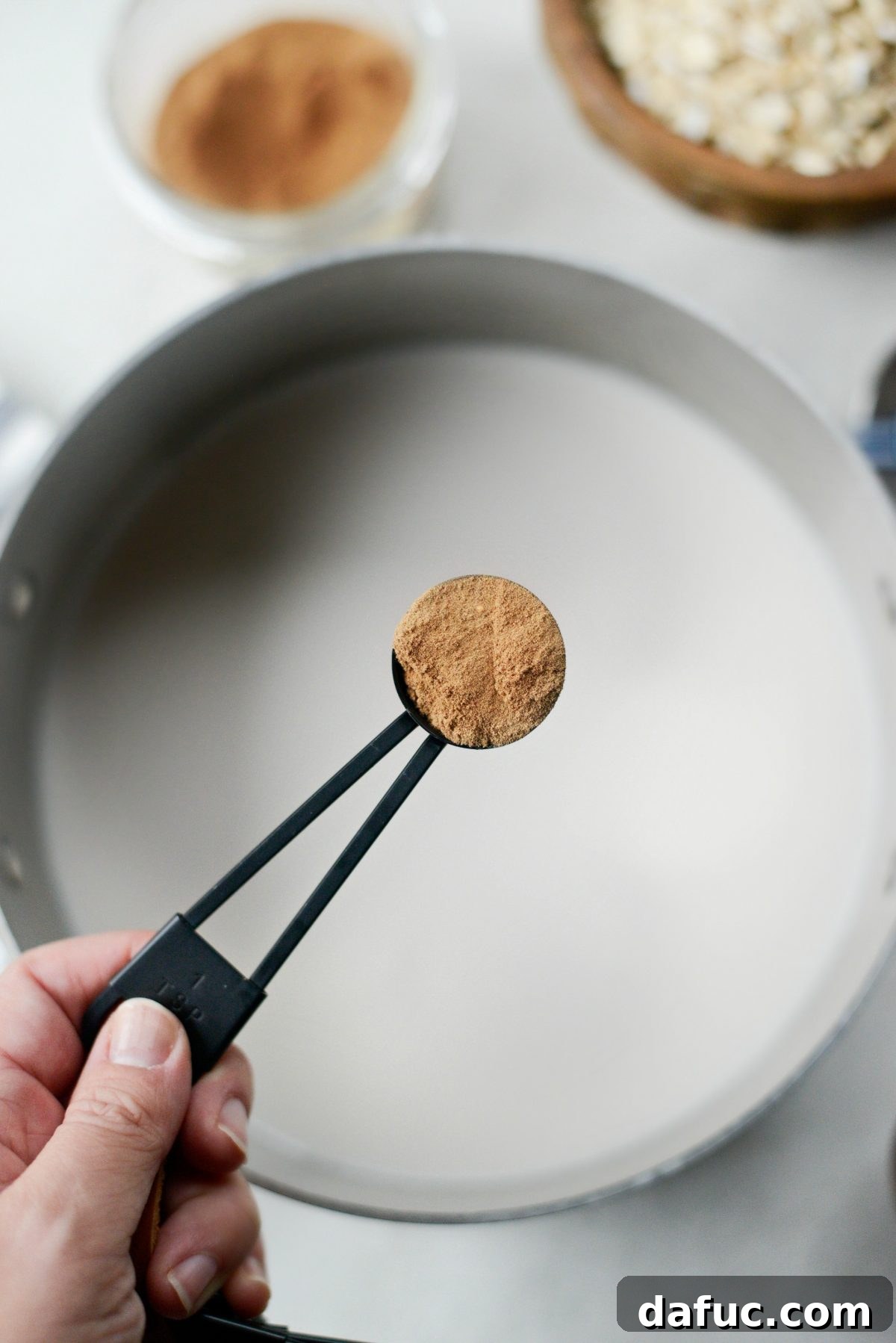 Adding a spoonful of homemade chai spice to the milk in the saucepan.