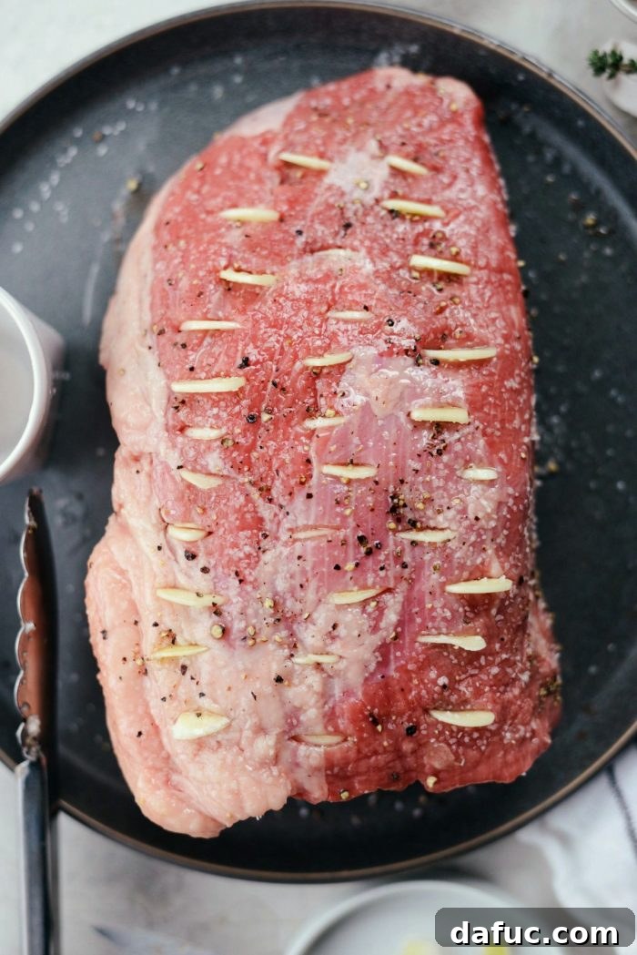 Inserting thin garlic slices into the prepared slits in the beef roast.