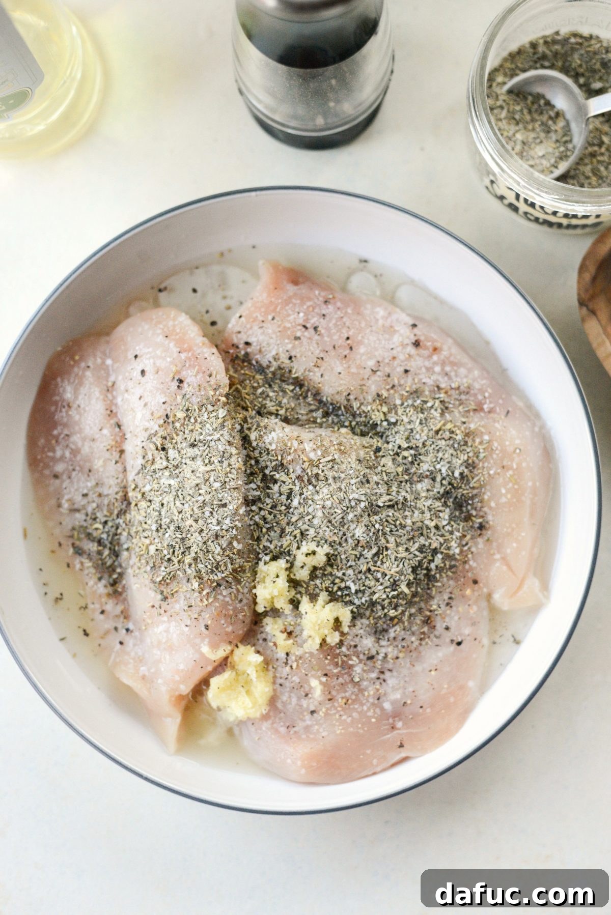 Chicken breasts marinating in a bowl with olive oil, lemon juice, grated garlic, and dried Tuscan herbs