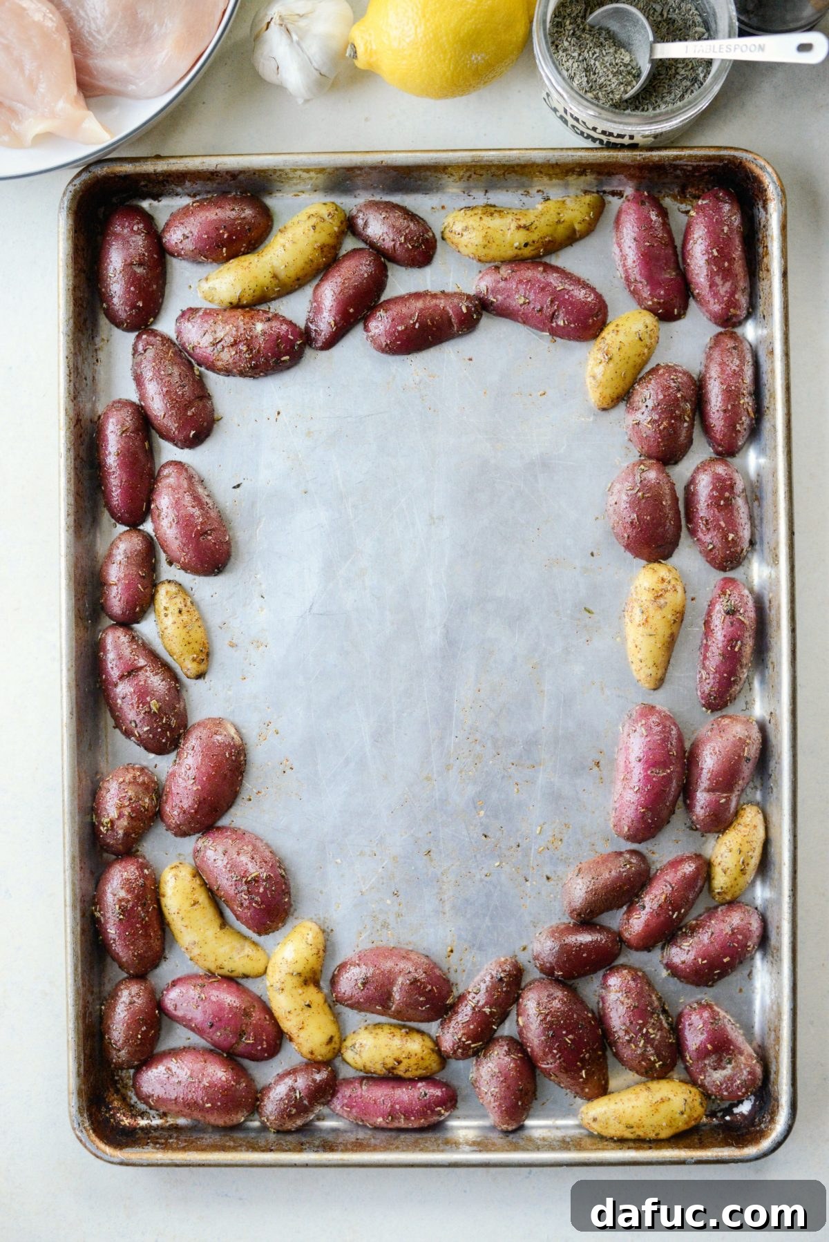 Arranging seasoned fingerling potatoes around the edge of a rimmed metal baking sheet for roasting