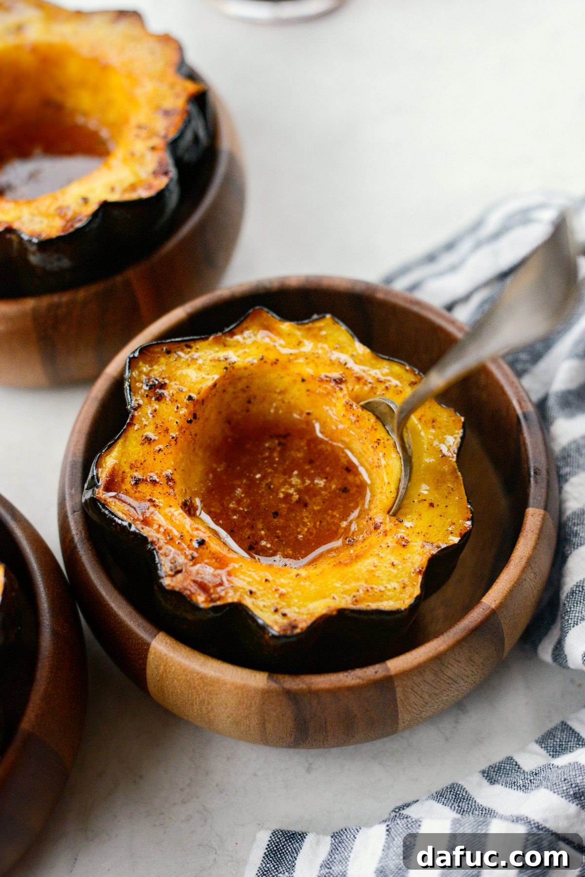 A spoon gently digging into the soft, caramelized flesh of a maple butter roasted acorn squash, highlighting its tenderness.