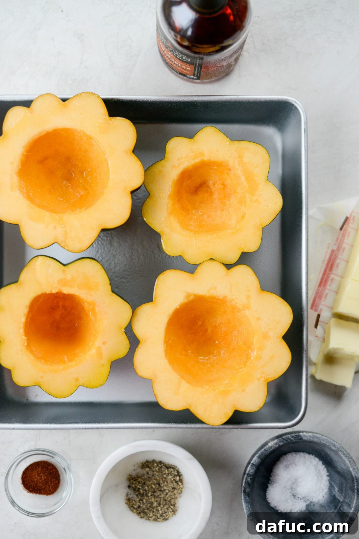 Two halves of acorn squash placed in a roasting pan, lightly sprayed with olive oil, ready for seasoning and roasting.