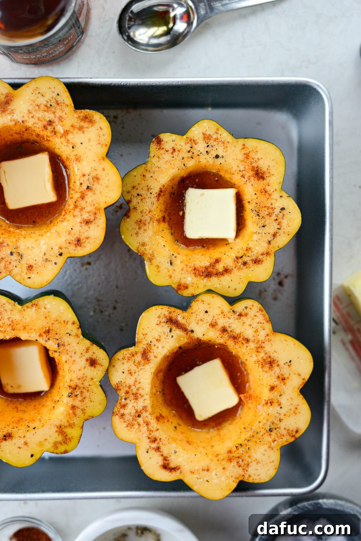 Butter and spices, including kosher salt, black pepper, and paprika, added to the maple-filled cavity of acorn squash halves.