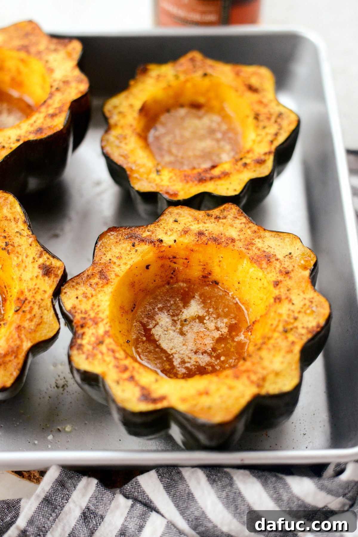 Acorn squash halves, seasoned and filled with maple syrup and butter, roasting in the oven, beginning to caramelize.