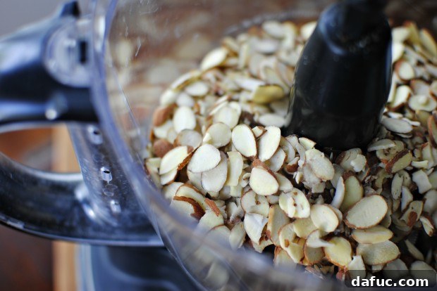 Sliced almonds in a food processor, ready to be ground