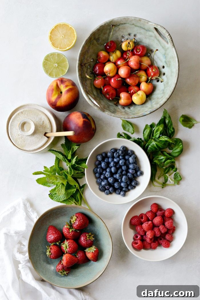 A beautiful arrangement of fresh ingredients for summer fruit salad: peaches, cherries, strawberries, blueberries, raspberries, mint, basil, honey, and citrus