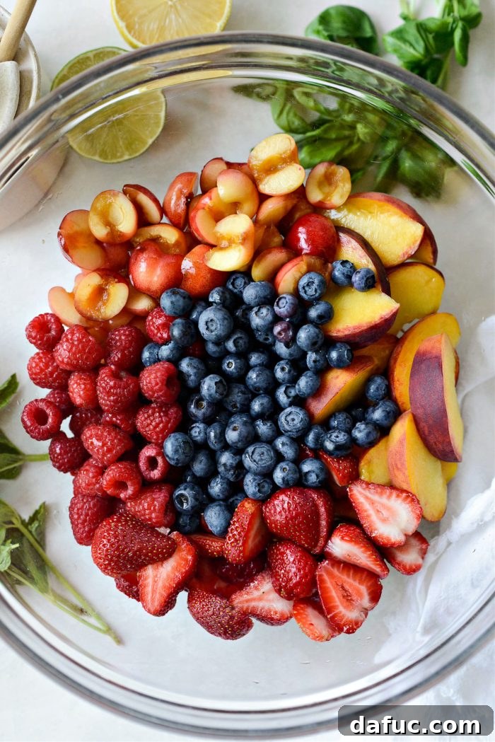 Adding perfectly sliced peaches, pitted cherries, and a mix of fresh berries into a large mixing bowl