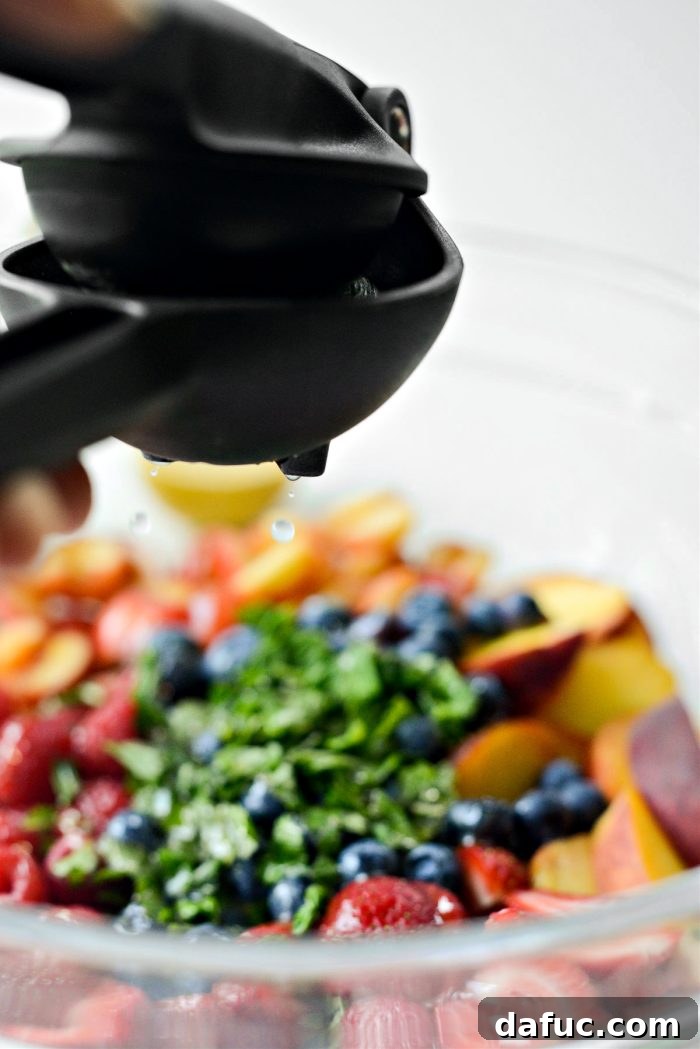 Squeezing fresh juice from half a lemon and half a lime directly over the mixed fruit and herbs