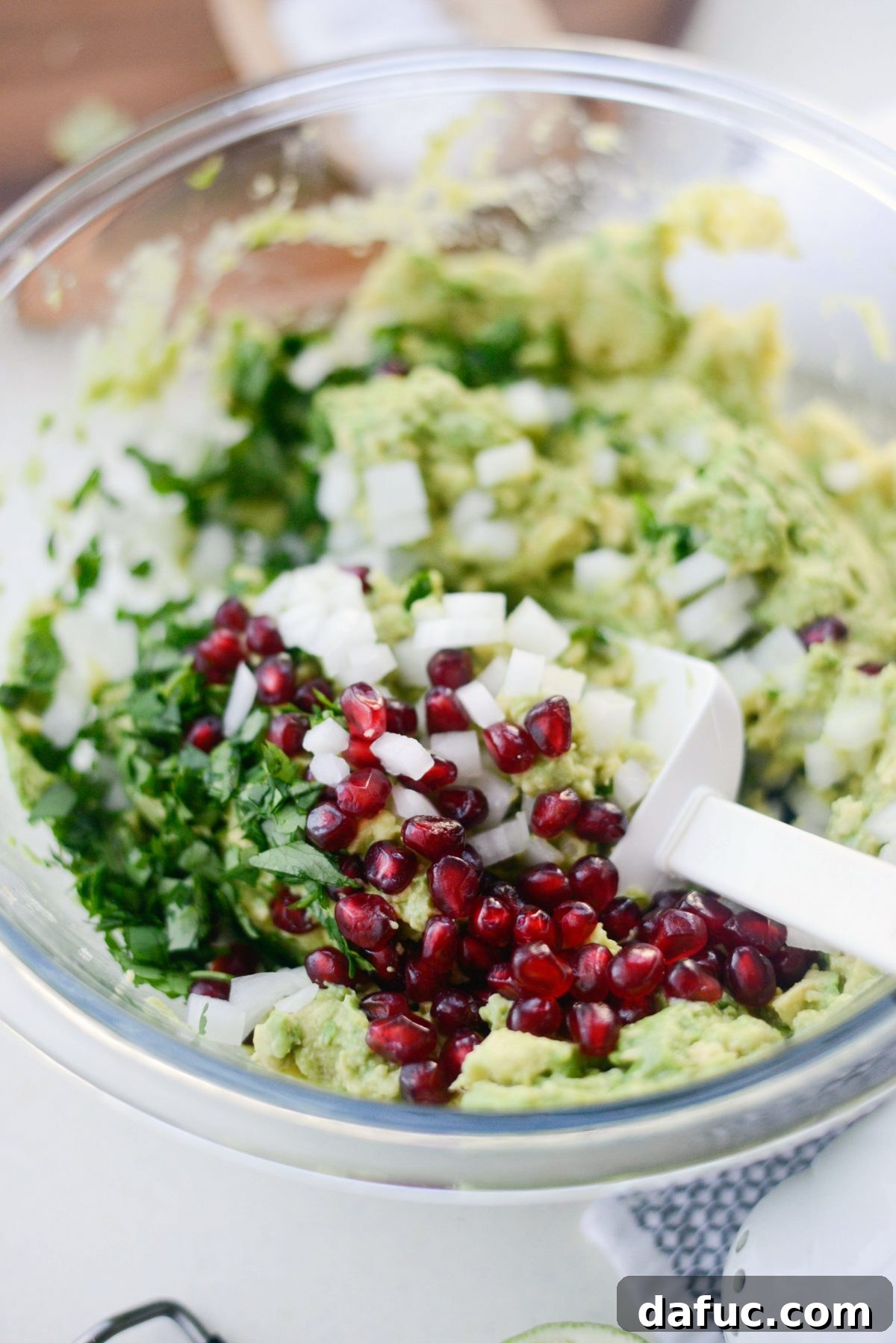 Using a spatula to gently combine all Holiday Guacamole ingredients