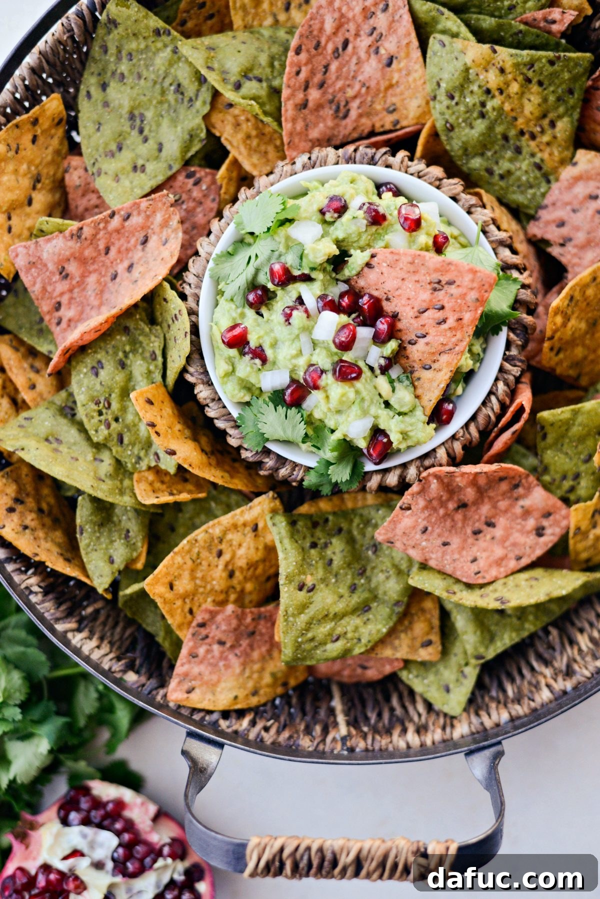 Tortilla chip dipped into creamy Holiday Guacamole with visible pomegranate seeds