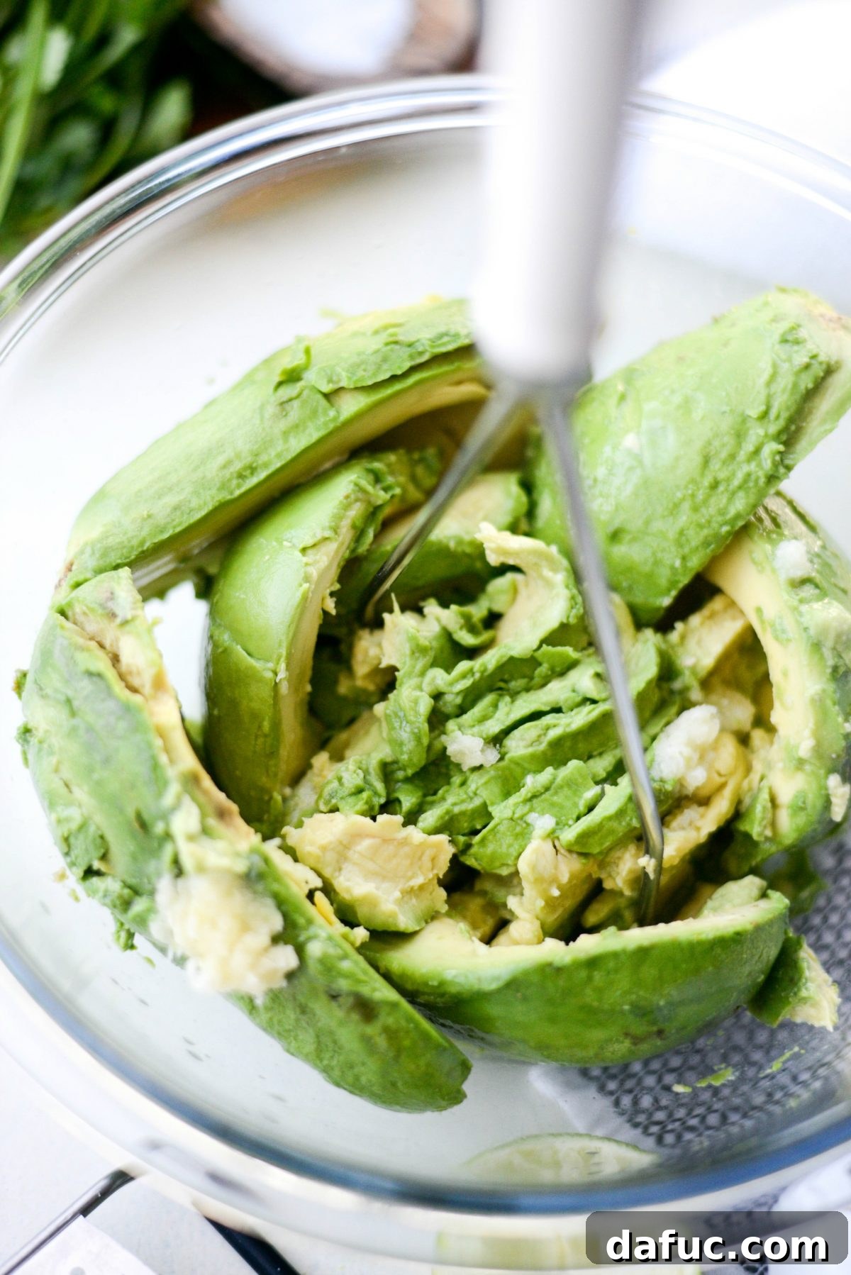 Mashing avocado, lime juice, and garlic together with a potato masher