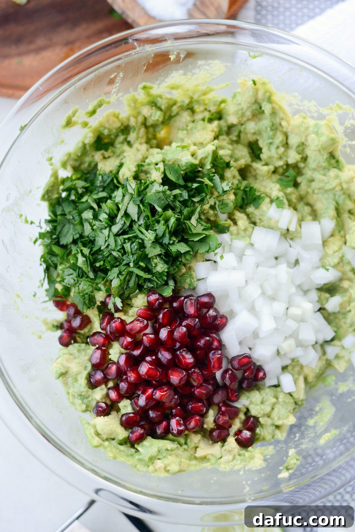 Adding pomegranate arils, diced white onion, and chopped cilantro to the mashed avocado
