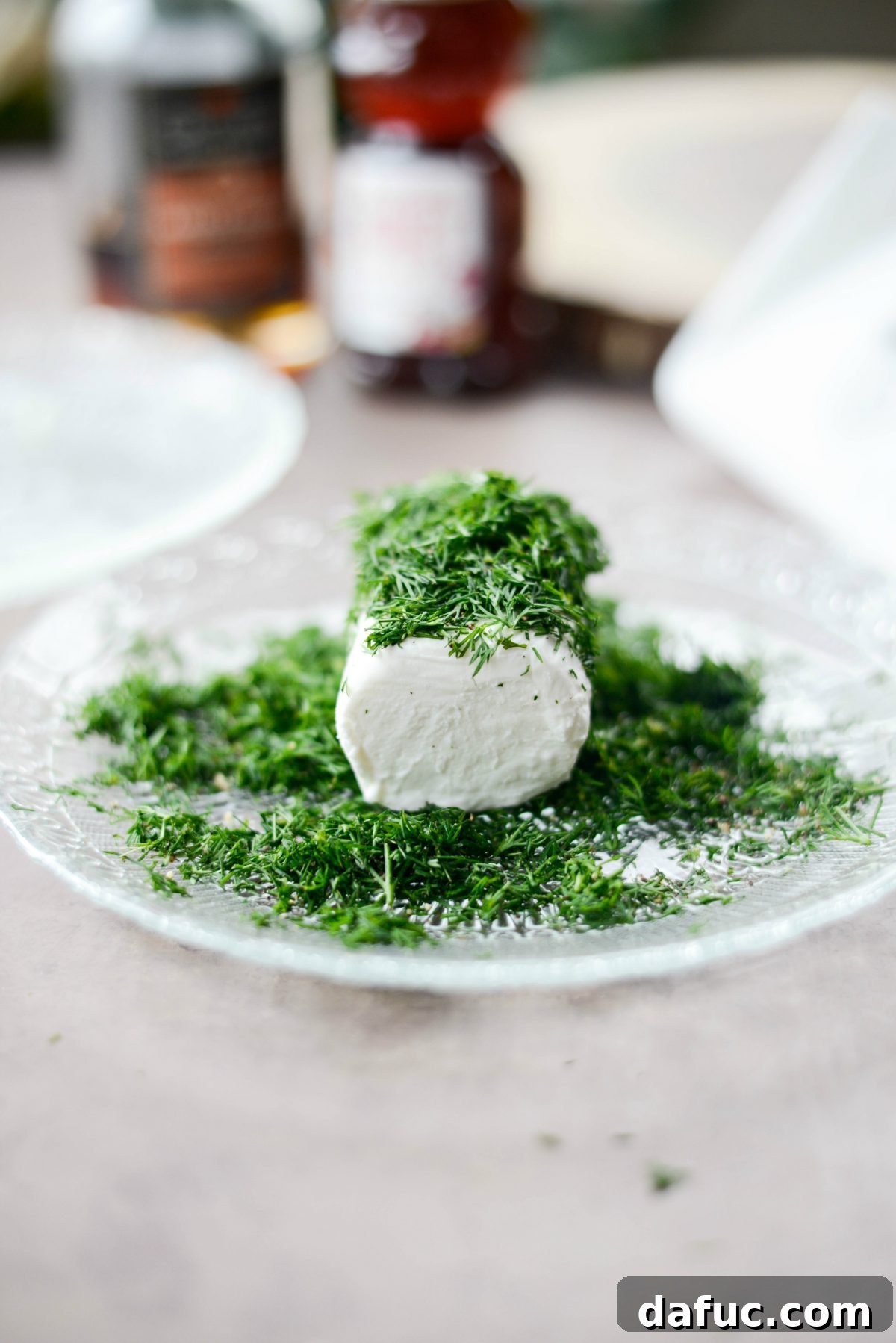 Goat cheese log being rolled in fresh dill and black pepper